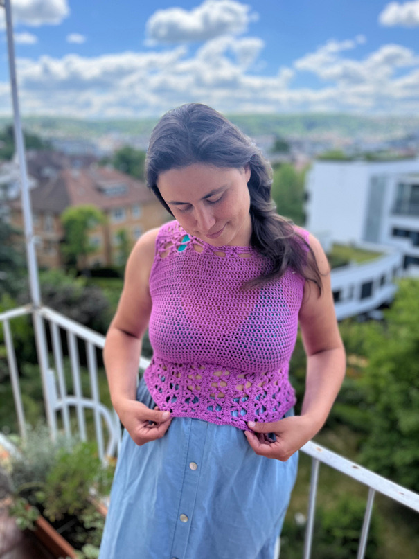 Steffi auf einem Balkon, sie trägt ein selbst gehäkeltes Top in Pink und schaut daran herunter